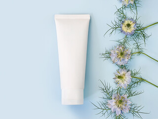 Unbranded white squeeze bottle cosmetic cream tube and line frame border of blue Nigella flowers on...
