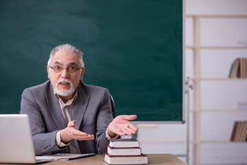 Old male teacher in front of blackboard