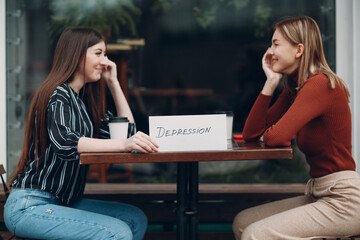 Hidden depression concept. Woman holding white sheet paper labeled word Depression in hand. Two women talking and smiling in street cafe