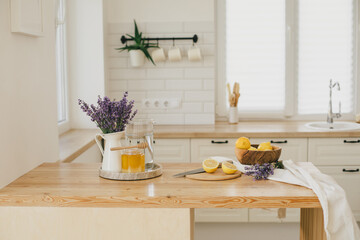 Fresh lemons, jar with honey and bunch of lavender flowers in a vase standing on a kitchen table at...