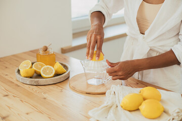 Young woman making lemonade in a kitchen of cozy house. Homemade healthy drink.