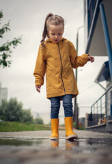 a girl in a raincoat and yellow boots walks through the puddles