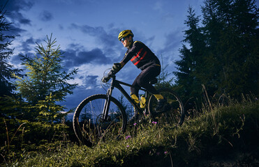 Young man riding bicycle downhill with beautiful blue evening sky on background. Male bicyclist in...