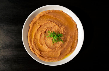 Famous traditional Arabic cuisine - peeled fava beans mashed plain in a white bowl on dark brown background. Top view. Foul Mudammas