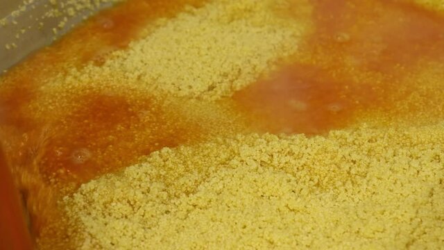 Close-up putting hot broth into couscous in metal tray. Cooking at commercial kitchen.