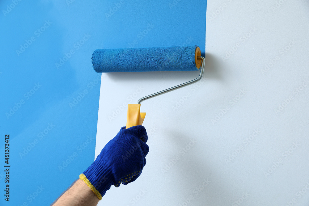 Sticker Man applying light blue paint with roller brush on white wall, closeup