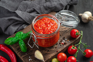 Tomato sauce in a glass jar on the background of ingredients.