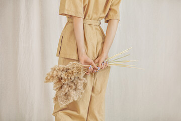 Young girl model in a pantsuit with her back on a linen background with spikelets in her hands close-up