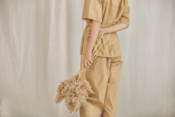 Young girl model in a pantsuit with her back on a linen background with spikelets in her hands close-up