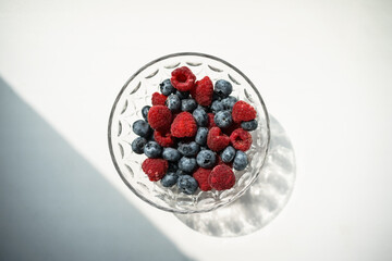 raspberries and blueberries in a transparent bowl on a white background