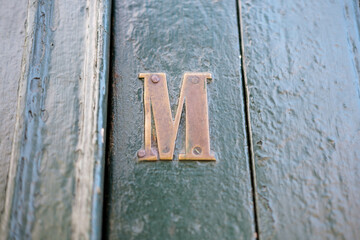 Brass captial letter M fitted to a rough green painted door