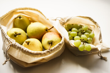 pears and grapes in white linen eco bags on a white windowsill