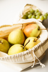 pears and grapes in white linen eco bags on a white windowsill
