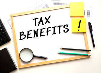 TAX BENEFITS text is written on a white office board. Work table with office supplies.