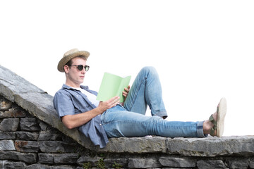 Handsome young man wearing a hat reading a book laying on a stone wall