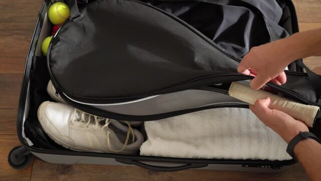 A professional tennis player prepares to play and puts his racket in his travel luggage.