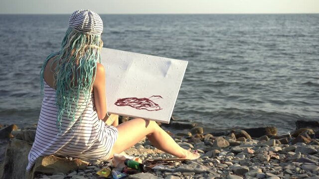 Young beautiful woman artist paints a picture on the wild sea shore