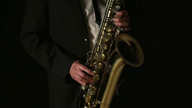 Musician plays saxophone in dark and is illuminated by the light in studio. Concept of playing the saxophone.