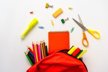 Eine rote Schultasche gefüllt mit bunten Schulartikeln auf einem weißen isolierten Hintergrund....