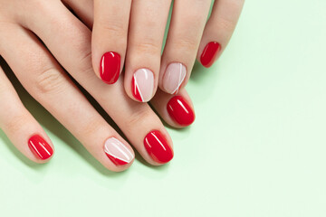 Women's hands with red, pink, white nail Polish applied on a light green background. Perfect artificial fingernails of young woman. Selective focus	