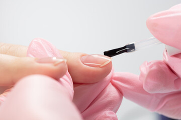 Close up process of applying clear varnish. Woman in salon receiving manicure by nail beautician....