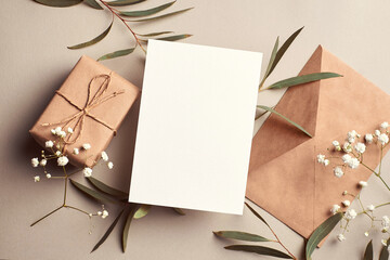 Greeting card mockup with gift box, envelope and eucalyptus and gypsophila twigs on beige...