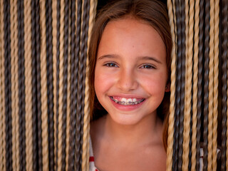 Portrait of a young caucasian girl with braces smiling through the curtains