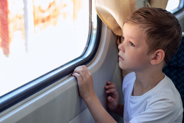 Fototapeta na wymiar A little boy looks out the train window. Summer close-up portrait. Travel.