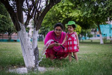 portrait of cute indian mother and daughter watering in the park.