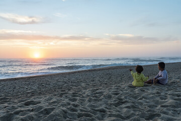 Fototapeta premium Two young caucasian kids at sunset on the northern beach in portugal pointing at the setting sun.