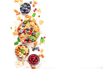 Fototapeta na wymiar Sugarless muesli in bowl and ingredients for healthy breakfast. Granola, nuts, blueberry, cranberry, greek yoghurt, whole grain flakes on white table, top view