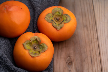 柿、木の板とグレーのタオルの上にのせた柿の写真