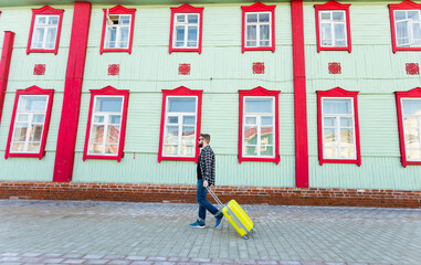Full body side portrait of happy travel man with suitcase walking along the building in city.