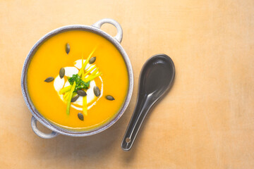 Pumpkin soup flavored with pumpkin seeds and yogurt in a ceramic blue  bowl with ceramic spoon on...