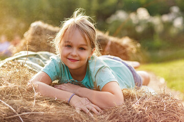 Portrait of a smiling 9-year-old blonde girl lying on a haystack. Happy childhood. A hot summer...