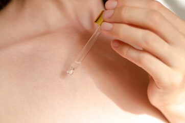 A woman's hand drips serum or essential oil onto her body from a pipette. Body care. Natural cosmetic
