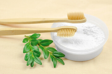 Bamboo toothbrushes and tooth powder with green leaves lie on a linen material. Eco-friendly products, no waste and no plastic. Zero waste. Eco-friendly self-care
