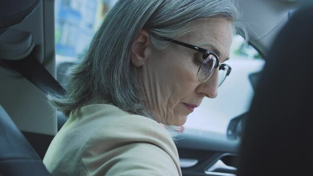 Serious concentrated woman getting into car, fastening seat belt going meeting