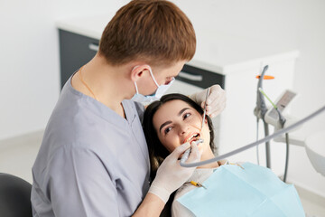 Fototapeta premium Beautiful young woman doing tooth examination in the dental office. Portrait of smiling girl on a dental chair in dentistry
