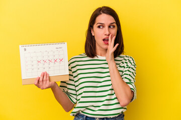 Young australian woman holding a calendar isolated on yellow background is saying a secret hot...