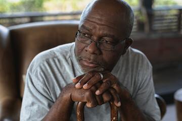 Thoughtful senior african american man sitting and leaning on the walking stick