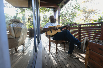 Senior african american man on sunny balcony playing the guitar