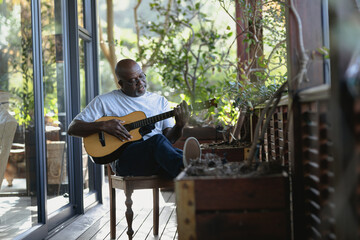 Relaxing senior african american man on sunny balcony playing the guitar