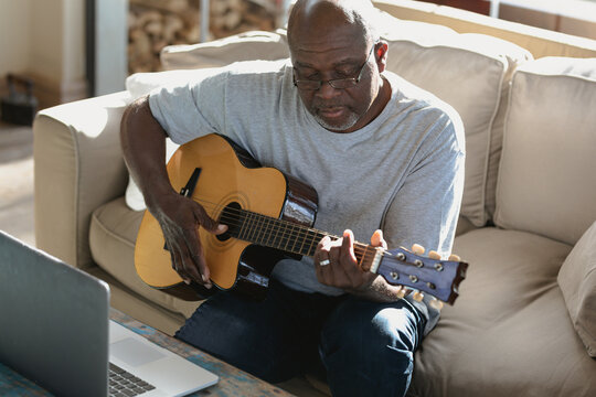 Senior african american man in the modern living room siting on the couch and playing the guitar