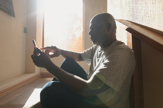 Thoughtful senior african american man siting on the sunny stairs and using smartphone