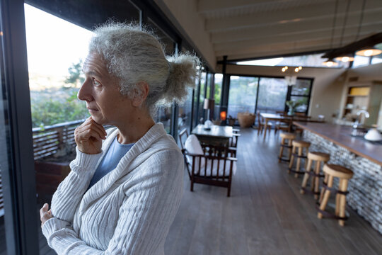 Thoughtful senior caucasian woman in kitchen standing and thinking
