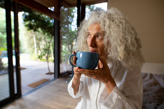 Thoughtful Senior Caucasian Woman Sitting On The Bad And Drinking Coffee