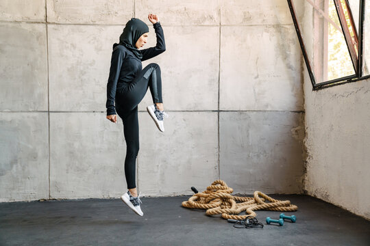 Young muslim woman in hijab jumping while working out indoors