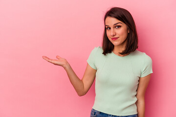 Young caucasian woman isolated on pink background showing a copy space on a palm and holding another hand on waist.