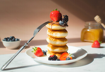 Cottage cheese pancakes with strawberries and blueberry on a pink background with shadows. Breakfast or lunch concept.